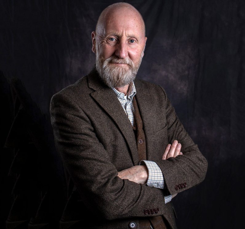 Stuart McAlister of Media by McAlister A bearded man in a brown blazer poses with arms crossed, smiling at the camera.